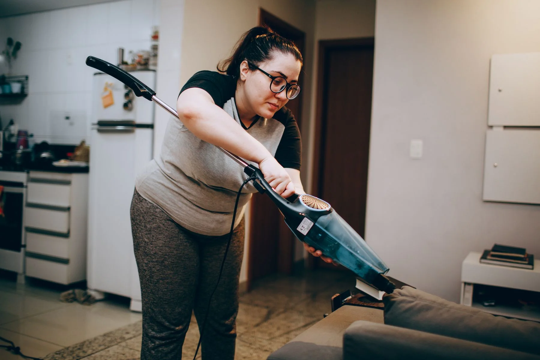 Person vacuuming a carpet beneath furniture.