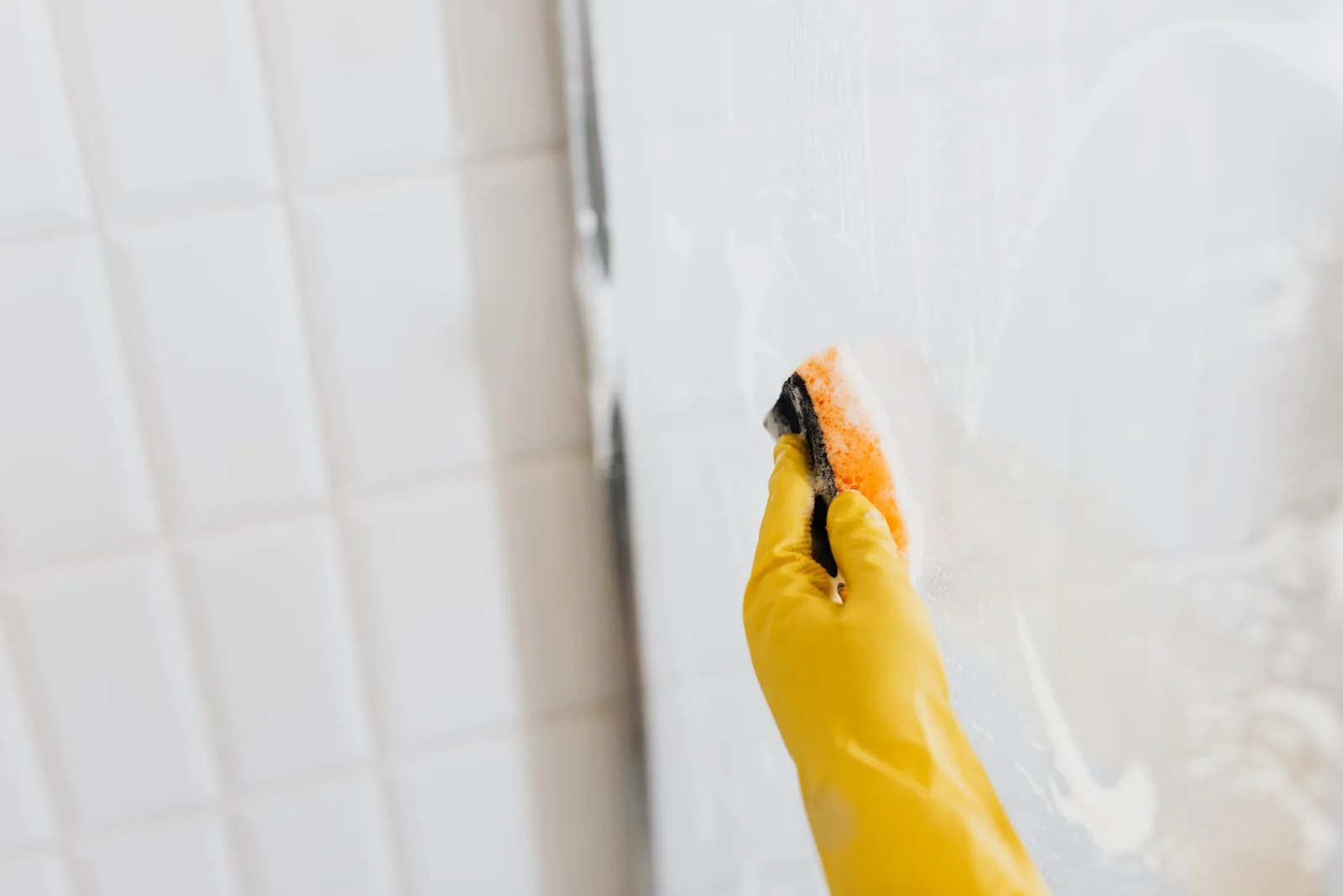 Gloved hand cleaning shower glass.