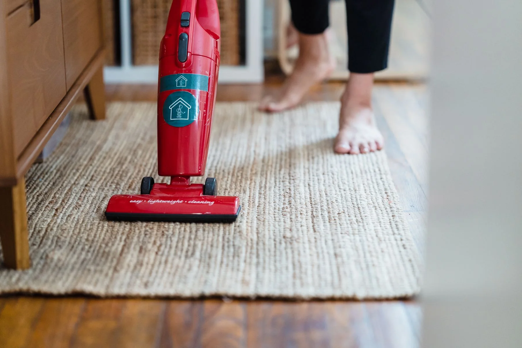 Person vacuuming carpet in a bright room.