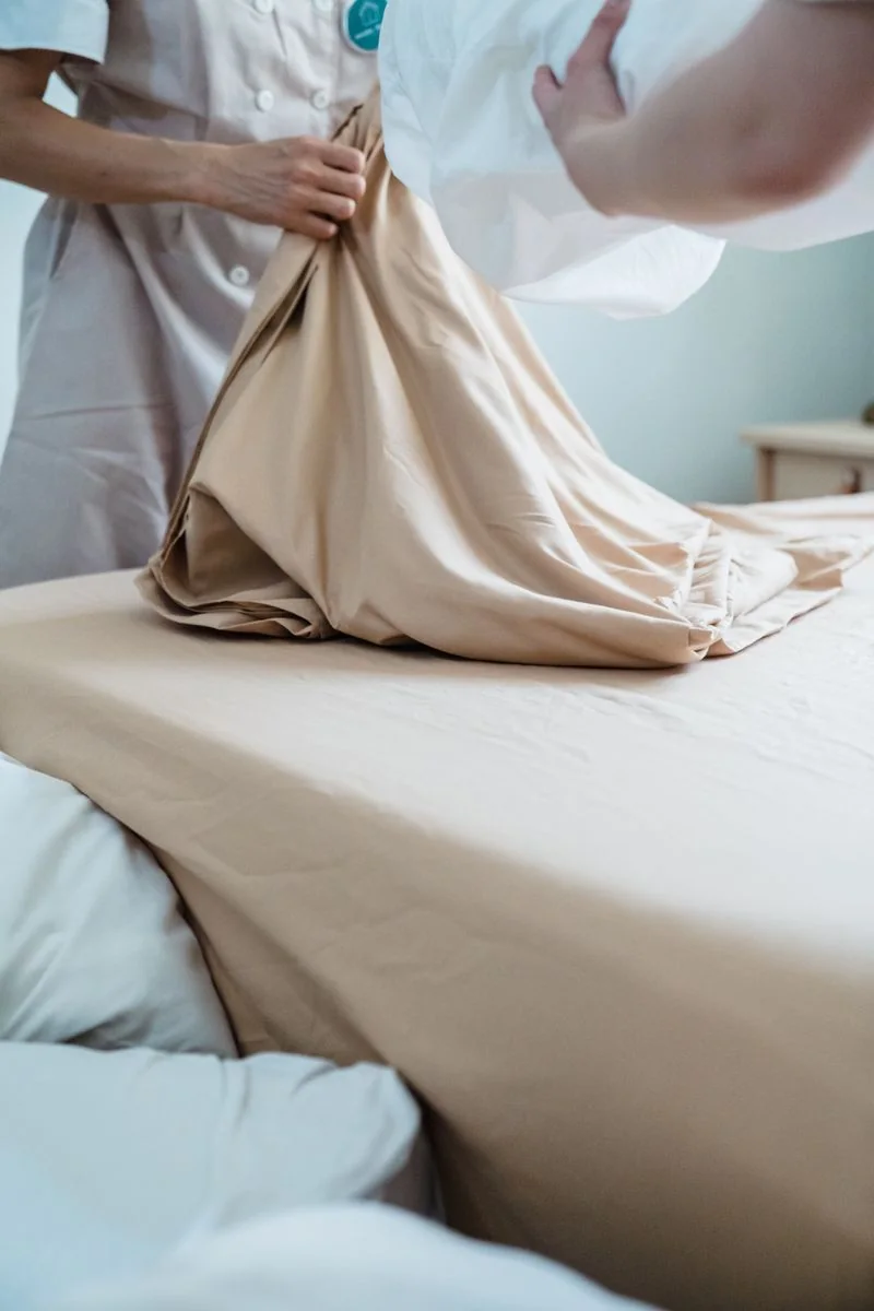 Housekeepers preparing fresh bedding in a guest room.